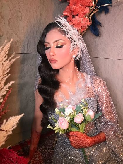 A modern Christian bride look. The makeup is soft and glamorous, with a focus on winged eyeliner and glowing skin, paired with a feathered headpiece.