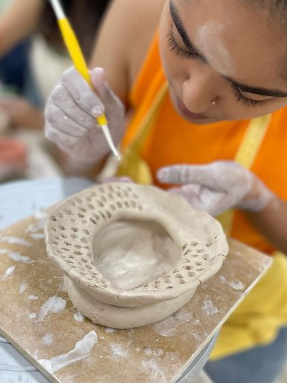 A student carefully pierces a pattern into the edge of their hand-built piece, a technique that requires patience and a steady hand.