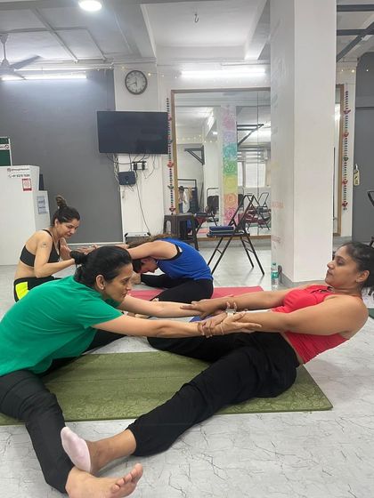 This assisted seated forward bend shows how we use partner work to increase flexibility and build trust among our students.