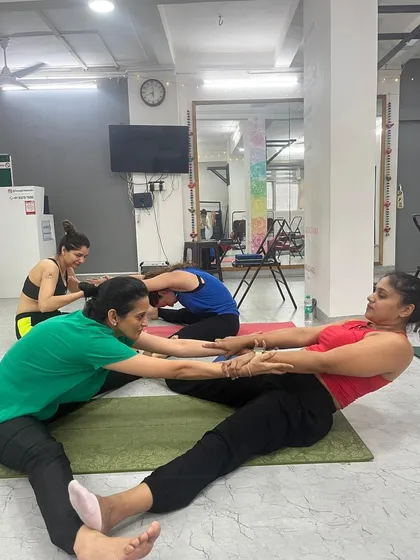 This assisted seated forward bend shows how we use partner work to increase flexibility and build trust among our students.