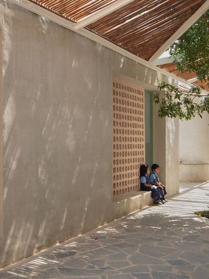 Students sit on a low wall outside their classroom, a space created by the building's form. The design incorporates informal seating and gathering spots throughout the campus.