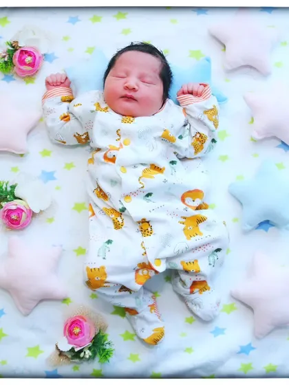 Twinkle, twinkle, little star. This peaceful newborn is sleeping on a star-patterned blanket, surrounded by soft star pillows and floral accents.