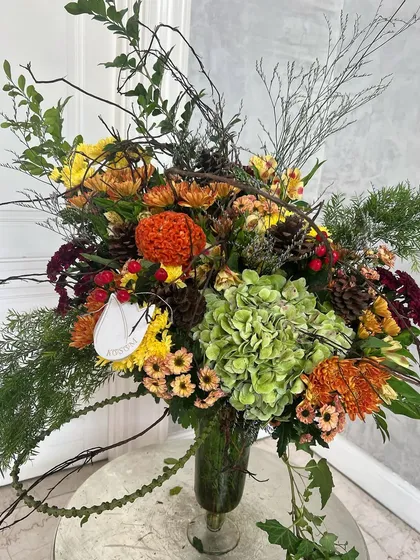 Crisp autumn colours. This arrangement features mustard yellow, pumpkin orange, olive green, and ruby reds, with wild woody stems and foliage for a rustic, seasonal feel.