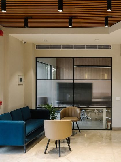 The waiting lounge on the ground floor uses a sophisticated palette of blues and beiges. Glass partitions maintain a sense of openness while separating the formal meeting areas.