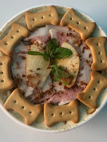 A close-up of my Apple & Bacon Pup Scoops. This dog-friendly ice cream is made with real ingredients, garnished with fresh apple, mint, and crunchy biscuits. It's a gourmet treat that's both delicious and healthy for your pup.