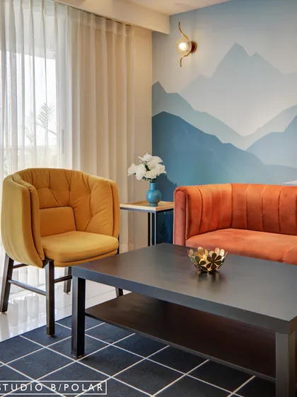 In this playroom, a beautiful mountain mural serves as a calming backdrop. We used brightly colored furniture, like the orange sofa and yellow armchair, to add personality and create a vibrant, inviting space for play.