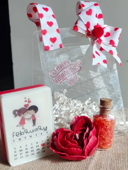 A sweet Valentine's Day gift set. This includes a calendar soap, a heart-shaped rose candle, and a bottle of bath salts, all in a cute gift bag.