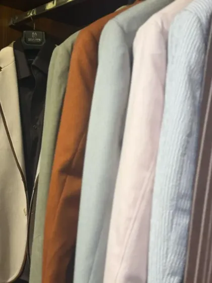 A rack of custom-made blazers and suit jackets in a variety of colors and fabrics, from classic pinstripes to solid pastels. Each one is ready to command a room with quiet expression.