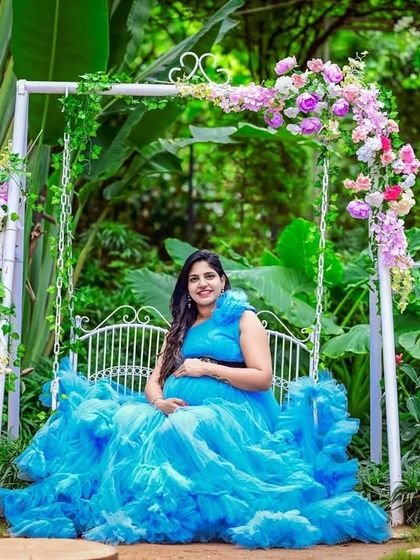 This blue ruffled gown looks stunning in a lush garden setting. The mom-to-be is seated on a decorated swing, creating a peaceful and pretty picture.