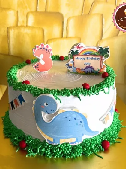 A cute dinosaur-themed cake for a third birthday. The design features a friendly blue dinosaur and green frosting borders, making it a perfect choice for a young dino fan.