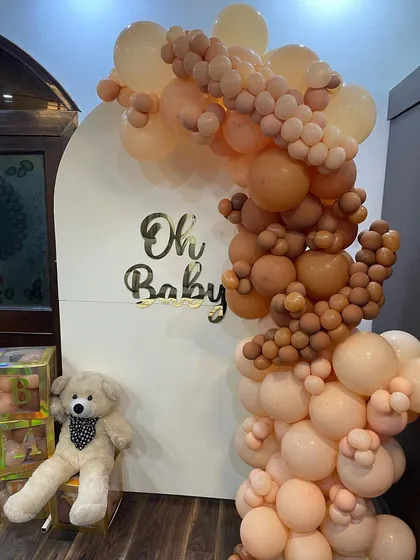 A modern and chic 'Oh Baby' shower decoration. We used a popular neutral color palette with a cascading balloon arch in shades of nude and brown against a clean white arched backdrop, perfect for a sophisticated Godh Bharai ceremony.