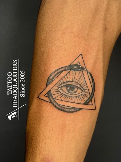 A tattoo of the Eye of Providence inside a triangle, encircled by an Ouroboros (a snake eating its own tail), rich in symbolism.