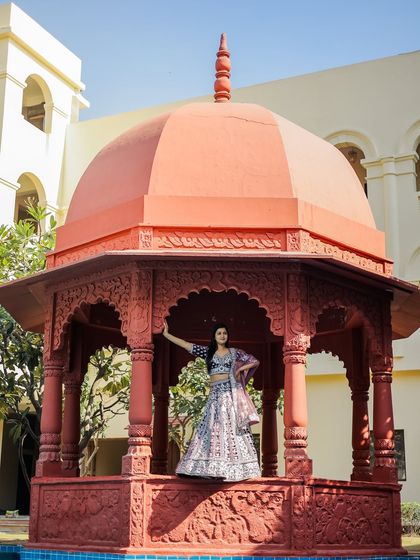 A stunning solo portrait of the bride in a gorgeous lehenga, posing inside a vibrant red gazebo at the Grand Imperial Hotel in Agra.