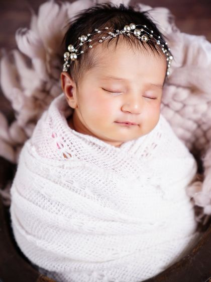 A close-up of a sleeping newborn wearing a delicate pearl headband, looking so serene and beautiful.