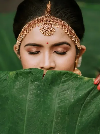 "Embrace the beauty within." A creative and artistic portrait of the bride, partially hidden by a large green leaf, focusing on her expressive eyes and traditional makeup.