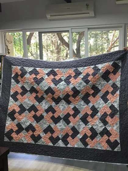 Two happy quilters holding up a finished quilt with a modern geometric pattern.