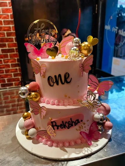 A two-tier pink butterfly-themed cake for a first birthday celebration.