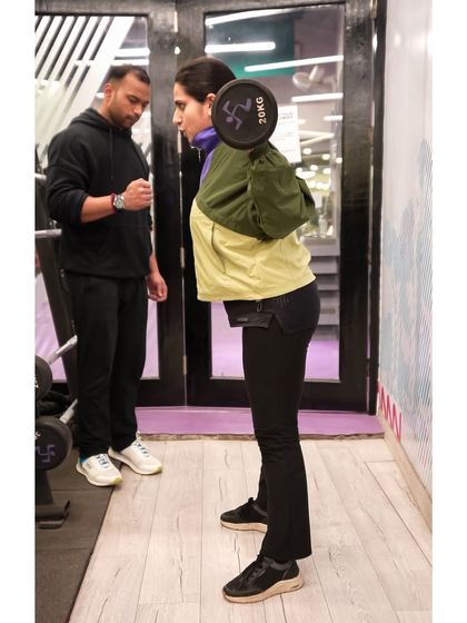A personal trainer carefully watches his client's form during a barbell squat, offering corrections and support to ensure a safe and effective lift.