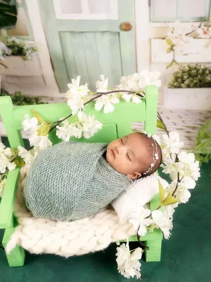 Sleeping on a tiny green bench adorned with white blossoms, this swaddled baby looks perfectly serene in a miniature garden setting.
