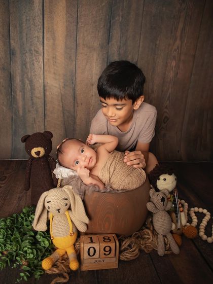 A proud big brother with his new sibling. This newborn portrait in our rustic wooden setup with cute stuffed animals creates a warm and timeless feel.