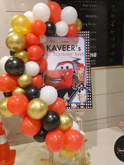 A welcome sign for a 3rd birthday 'Cars' themed party, with a balloon garland in the theme's colors.