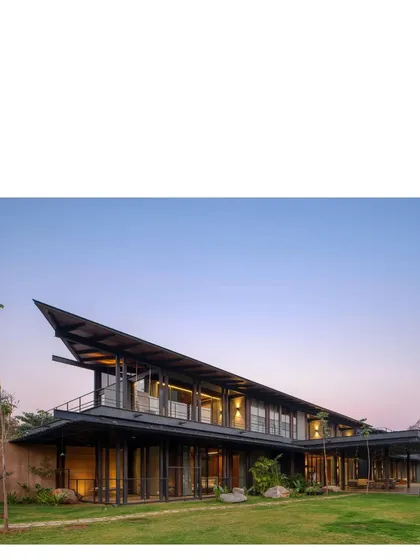 The house at dusk, with its warm interior lights glowing. The structure is designed to be a welcoming beacon in the vast landscape.