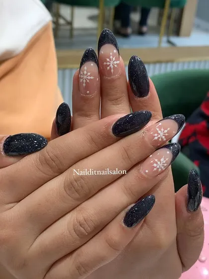 A winter-themed design featuring a deep, sparkling black glitter polish. Accent nails with a sheer base and hand-painted white snowflakes create a beautiful contrast.