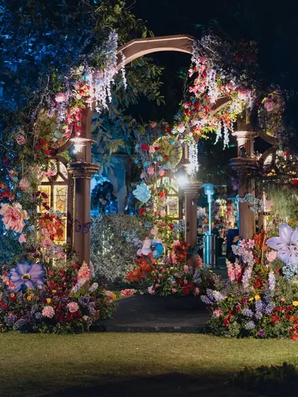 A fairytale-like entrance arch for a Sangeet, adorned with colorful flowers and featuring illuminated stained-glass-effect windows, creating a magical welcome.