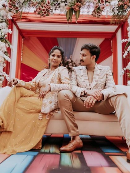 The couple posing on a couch against a colorful backdrop at their carnival-themed event.