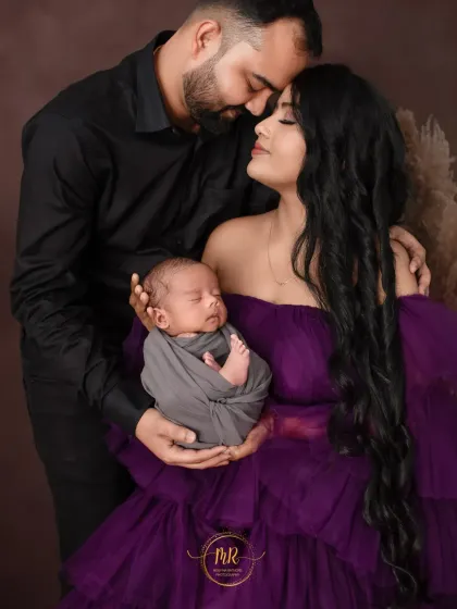 A close, loving family portrait. The parents hold their newborn baby together, their faces close in a tender moment.