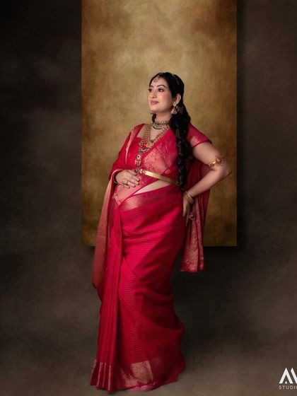 A full-length portrait of Tejaswini, glowing in a traditional red saree for her maternity shoot.