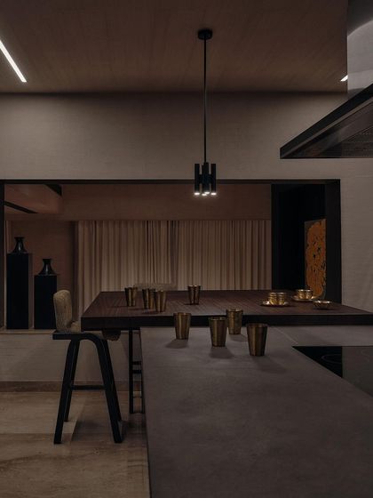 The kitchen island doubles as a breakfast bar, with brass glasses adding a touch of warmth to the cool, dark tones. The lighting is kept minimal and focused.