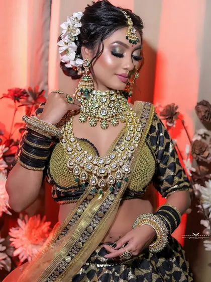 A graceful pose showing the bride adjusting her elaborate necklace, with white flowers in her hair.
