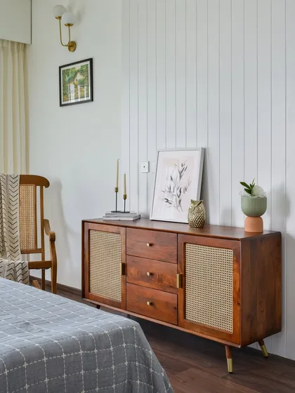 The master bedroom in 'Malhar' features a paneled wall that serves as a stylish backdrop for a sleek sideboard with cane-fronted doors.