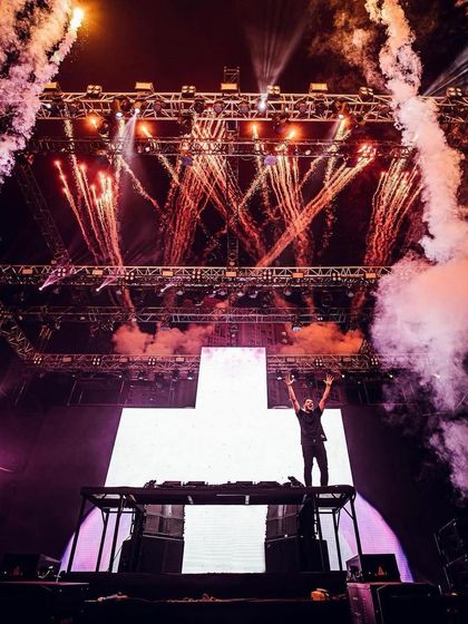 Martin Garrix stands before his signature cross logo, framed by an explosion of fireworks and CO2 cannons.
