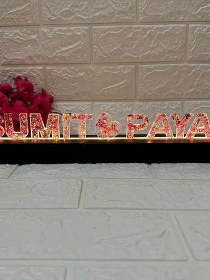 A frontal view of the name stand with the warm LED lights turned on, illuminating the preserved petals inside the letters.