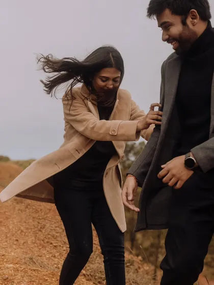 A candid and playful moment of the couple in the woods, with the wind catching the bride's hair as she holds onto her partner.