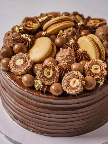 A celebration cake that screams indulgence. This shot for a baker captures the sheer decadence of a chocolate cake loaded with Ferrero Rocher and macarons. The lighting highlights the glossy texture of the frosting and the variety of toppings.