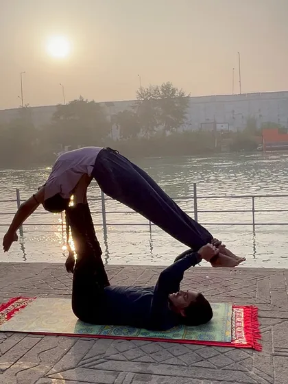 The 'superman' or front plank pose in acroyoga, silhouetted against the morning sun over the river in Haridwar.