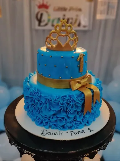 A royal blue two-tiered prince cake with a golden crown and ruffle details. It's a handsome and regal choice for your little prince's first birthday.