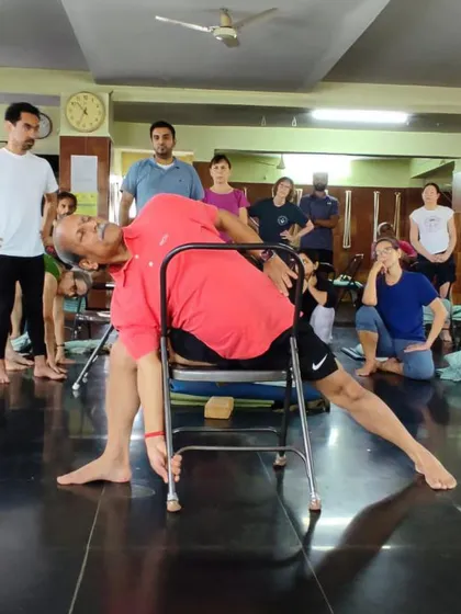 Demonstrating a lateral bend on a chair during a festival. This pose stretches the sides of the torso and improves flexibility in the spine.