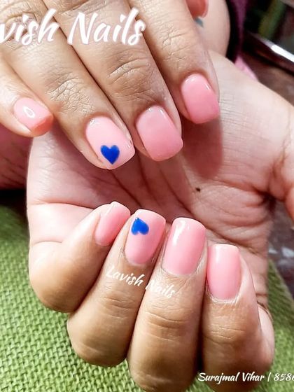 A simple and sweet light pink manicure on short, natural nails with a single, hand-painted blue heart accent.