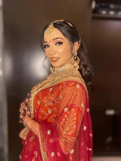 Purva embodies the royal Indian bride with this stunning look. The makeup features warm, earthy tones on the eyes and a bold lip to match her orange and red lehenga.