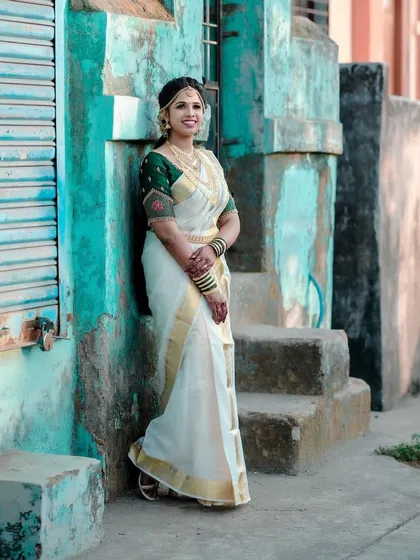 A beautiful shot of a bride against a rustic backdrop. Her traditional Kerala saree and joyful smile make for a perfect picture.