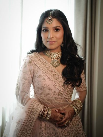 A portrait of timeless bridal elegance. Her pastel pink lehenga and soft, luminous makeup create a dreamy vibe that is perfect for a modern bride.