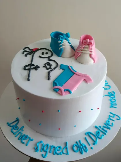 A funny and modern baby shower cake with a meme-style drawing and cute fondant baby shoes and onesie.