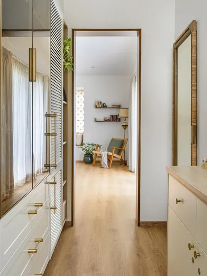 A view through the walk-in closet into the primary room of the 'House of Kismish' project. The combination of tinted glass and solid drawers provides both display and concealed storage.