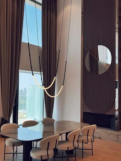 The Leda suspension light in a double-height dining space. Its flexible form, composed of cylindrical bars and a glowing silicone tube, can be installed in any direction to create a custom look.