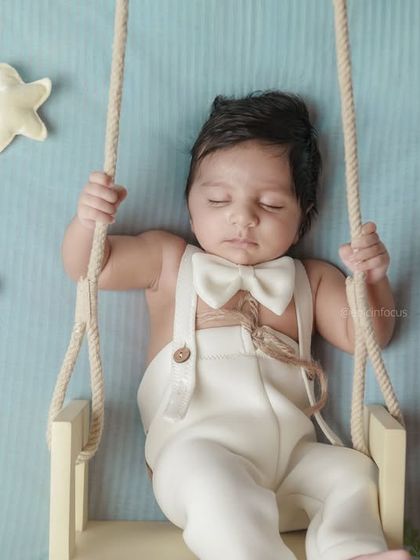 A celestial-themed shoot with a baby boy dressed in a bow tie, sleeping on a swing among plush stars and a crescent moon. This dreamy setup creates a magical, sky-inspired portrait.