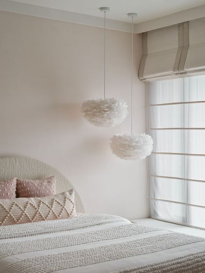 The bedroom is a cocoon of soft textures and colors, with fluffy pendant lights and layered textiles. The design creates a peaceful and comforting retreat.